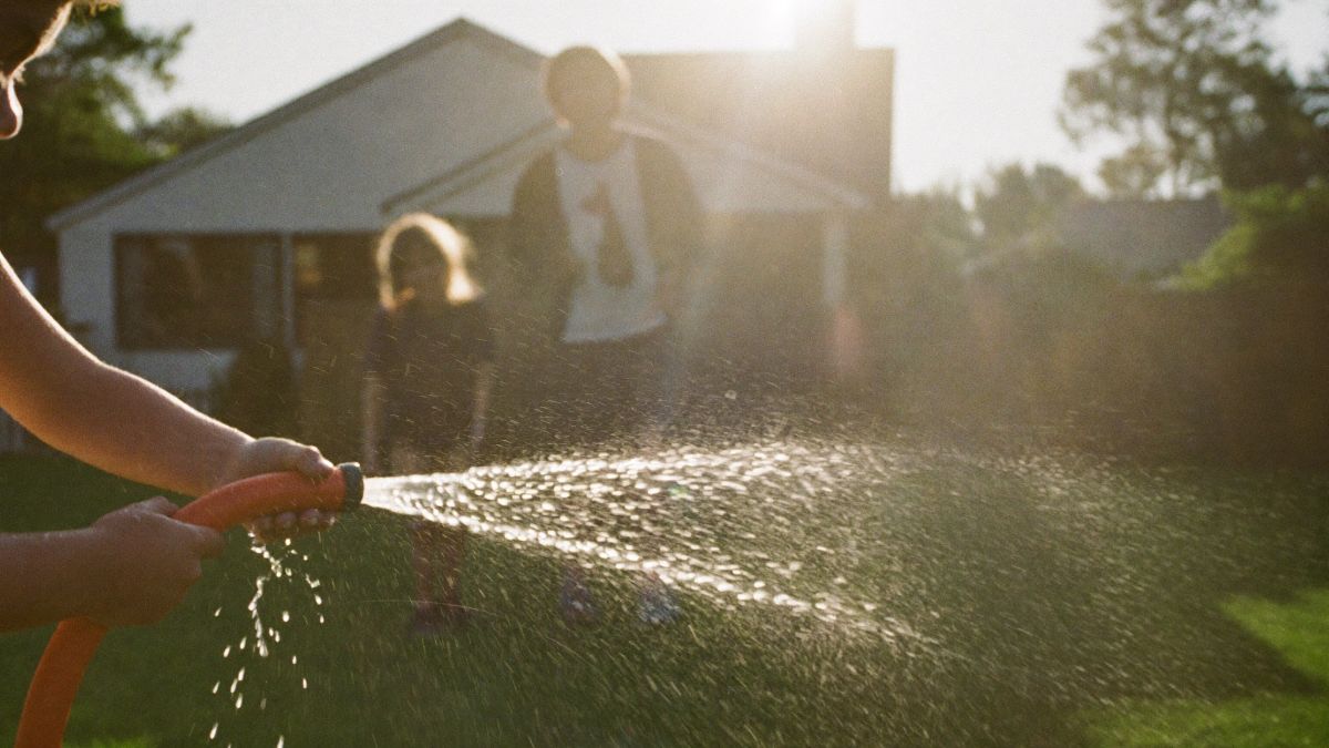 A child spraying a hose on a front lawn